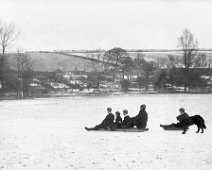 Mr. H. and children sledging Sedgeford park and houses along the Fring Road Original caption: Mr. H. and children sledging