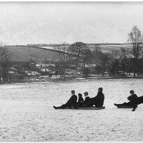 Mr. H. and children sledging Sedgeford park and houses along the Fring Road Original caption: Mr. H. and children sledging