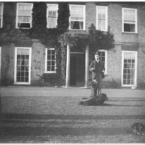 Father with dog & cat on lawn. Girl watching Sedgeford Hall Original caption: Father with dog and cat on lawn. Girl watching